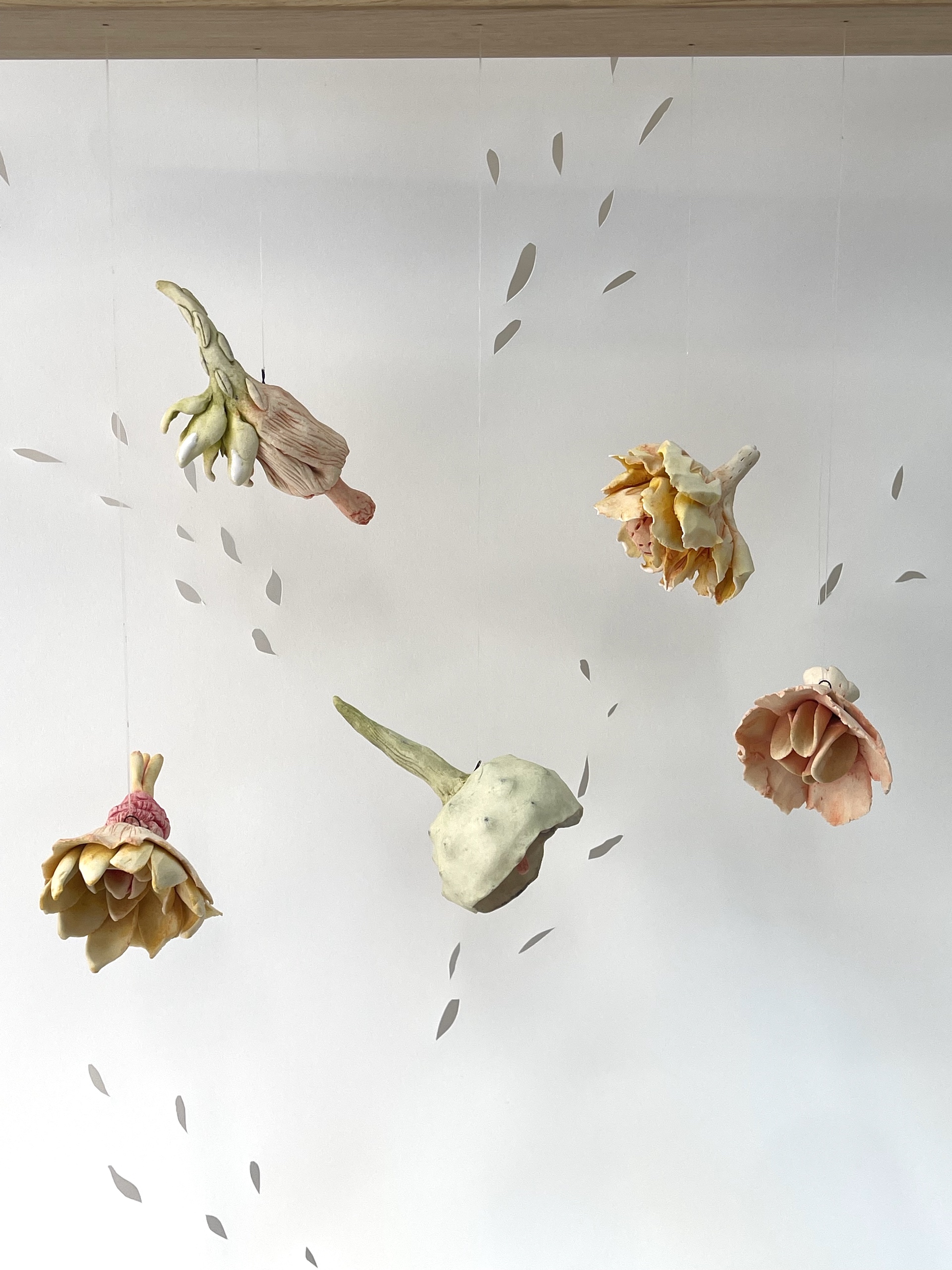 Ceramic flowers suspended against backdrop of paper-cut seeds.