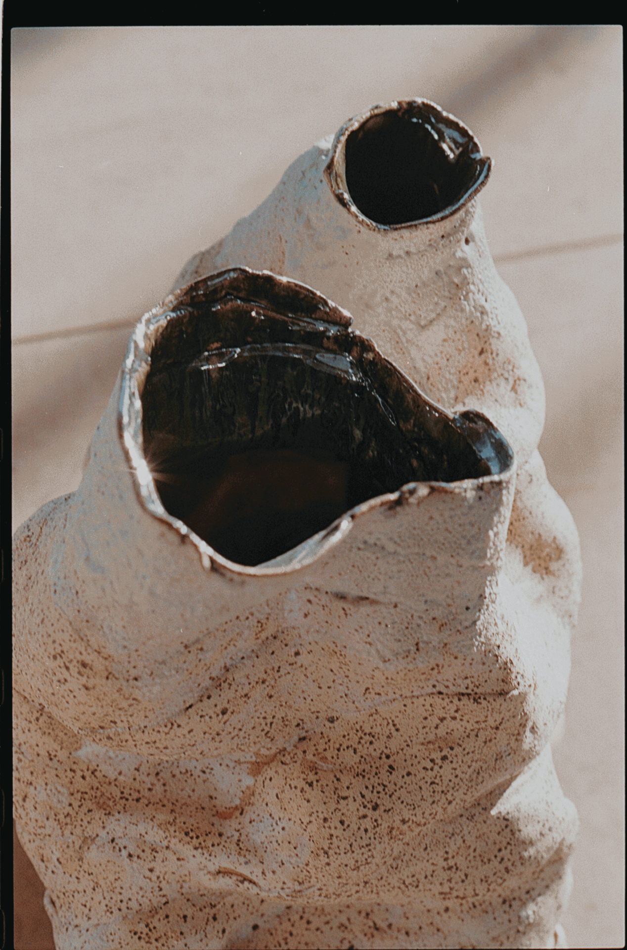 Closeup of handcrafted sculptural vase made of speckled stoneware with mirrored black interior glazing