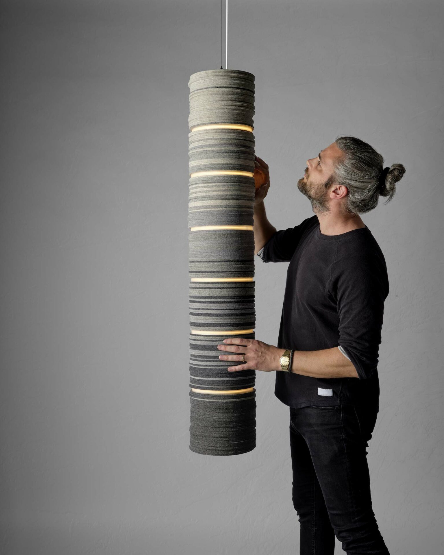 A man wearing black looking closely at a pendant light made from felt
