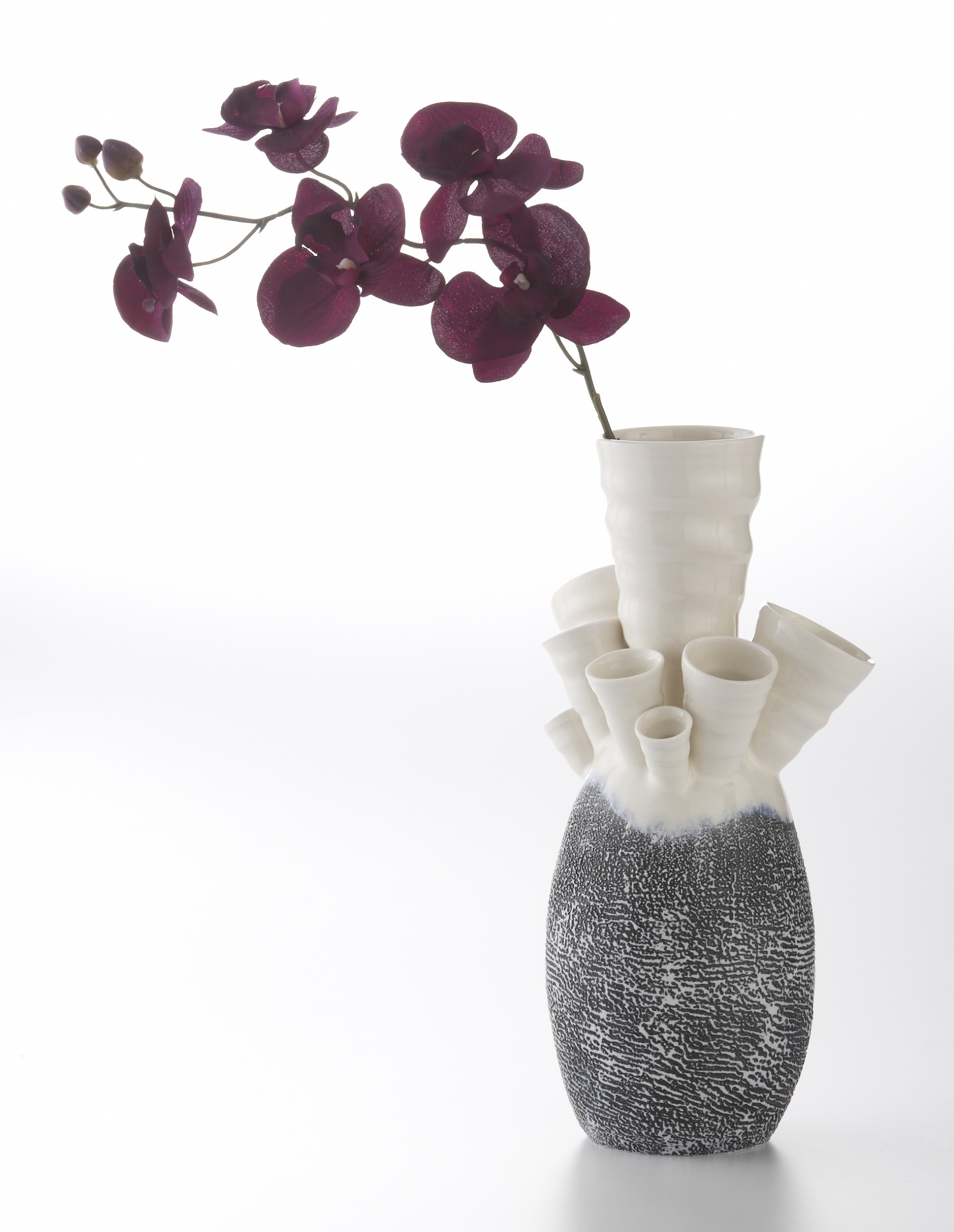 White tubular vase with black and white texture on the bottom and purple flower coming out of one of the tubes.