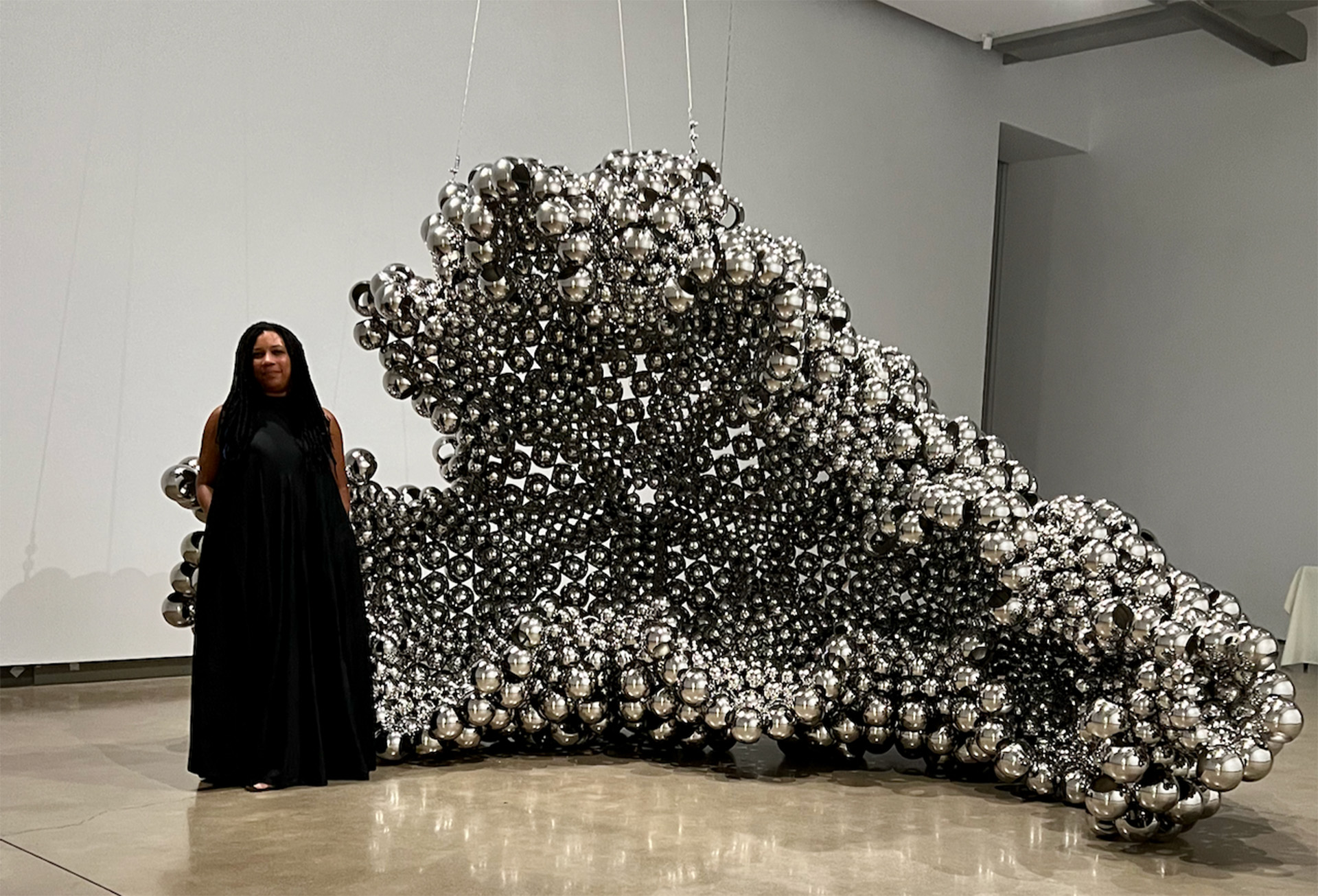 artist standing in front of large stainless steel beadwork sculpture