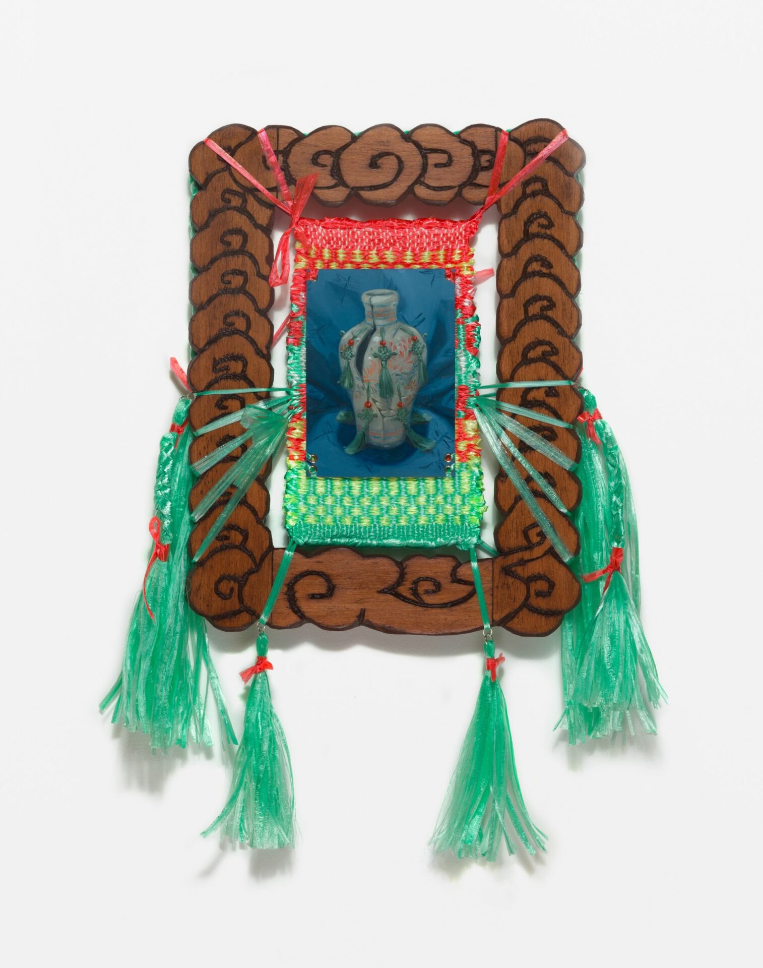 A painting of an Asian style jar, displayed in a carved wooden frame embellished with green ribbon