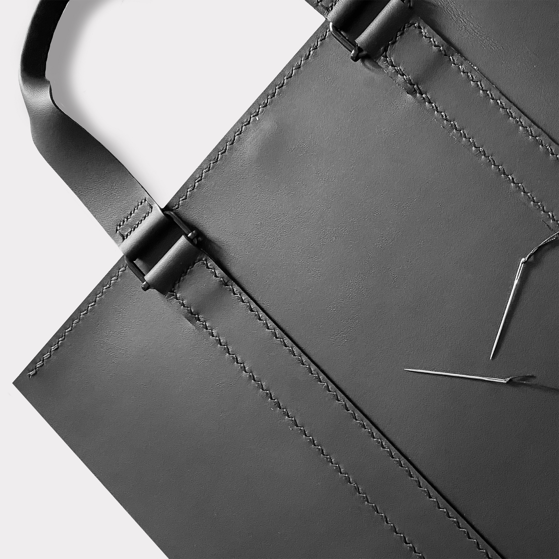 Black leather tote in stitching process on gray background.