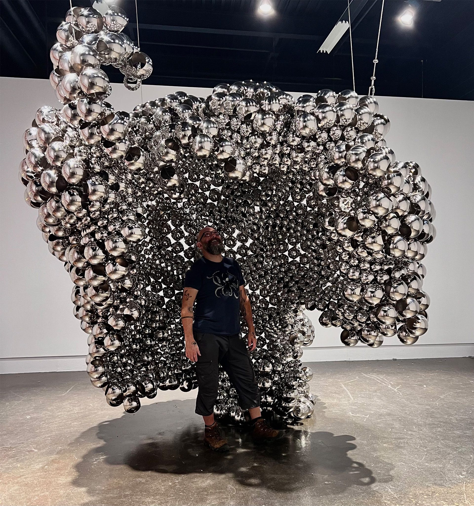 Man standing under a canopy of stainless steel spheres