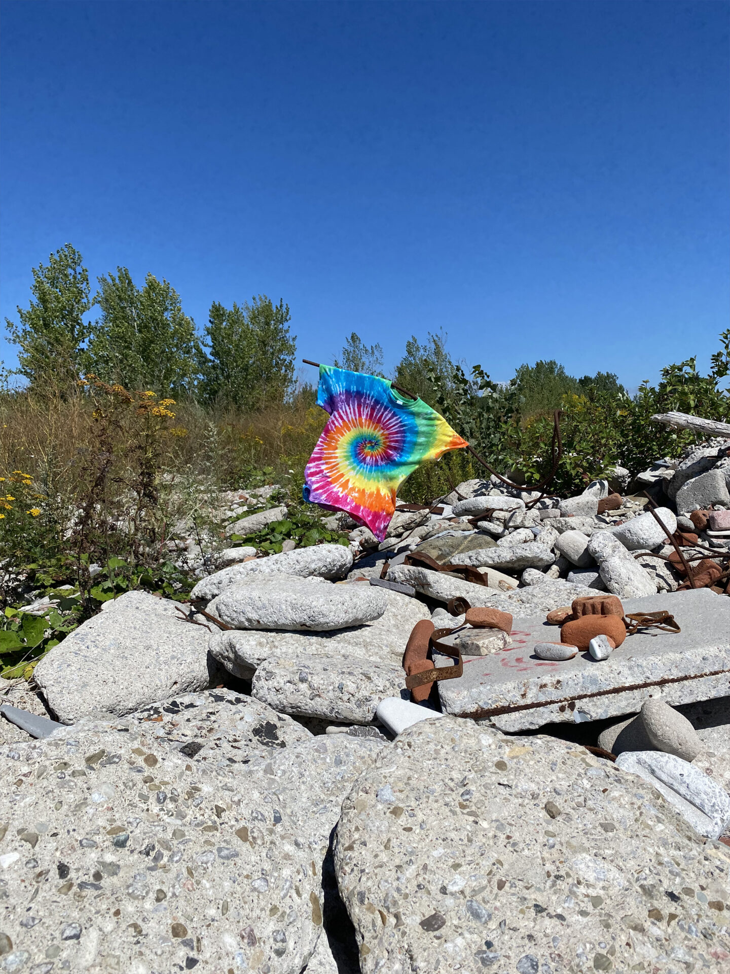 A rainbow tie-dyed t-shirt hangs on a piece of rebar surrounded by discarded building materials.