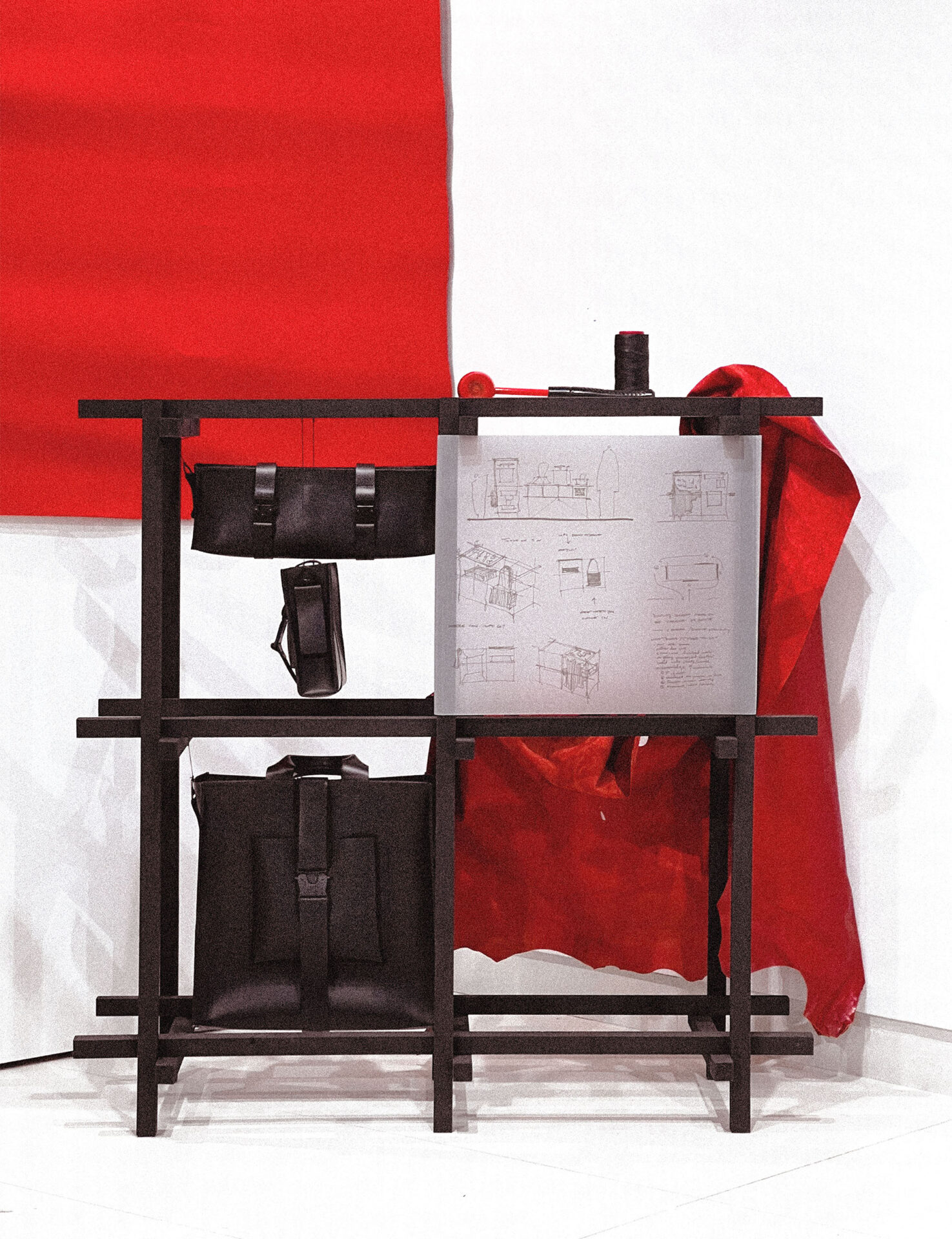 Display of black leather bags and trace paper sketches on a wooden frame armature.