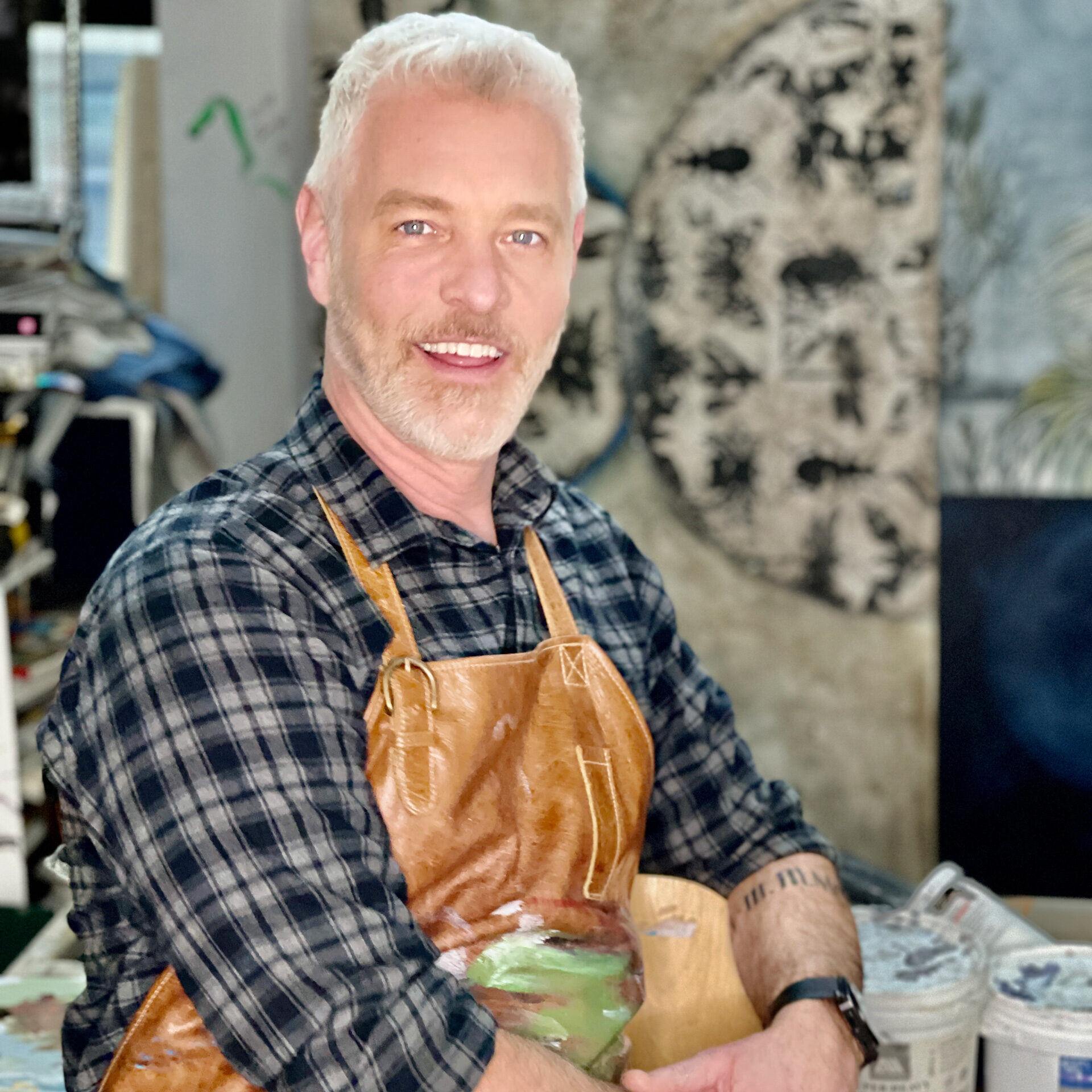 A smiling Caucasian man wearing a leather apron in his workshop